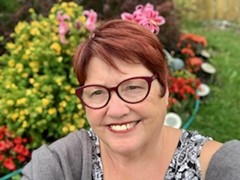 Dororthy, a woman with red hair and wearing glasses, smiles at the camera with flowers in the background
