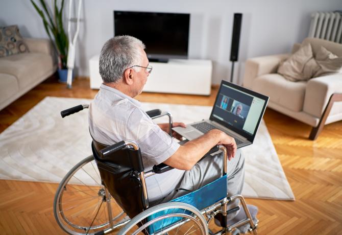 man in wheelchair looking a laptop screen taking part in online meeting