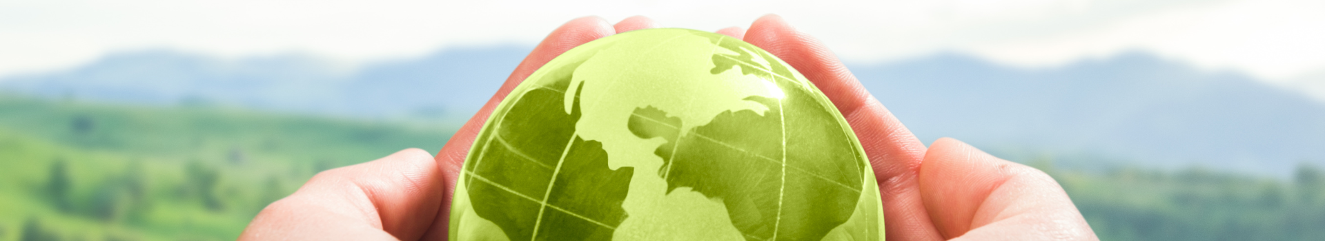 hands holding a small green globe in the foreground with rolling hills and grass in the background