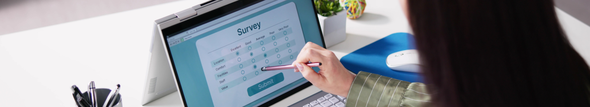 A person is back-on to the camera, working at a white desk with a laptop computer showing a survey.